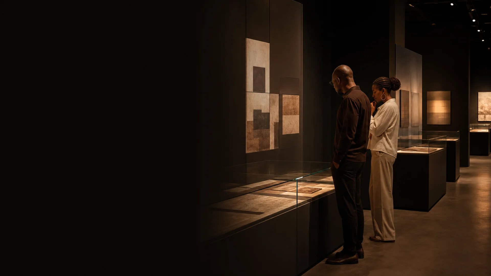 Deux visiteurs examinent des supports documentaires dans une galerie mémorielle contemporaine.