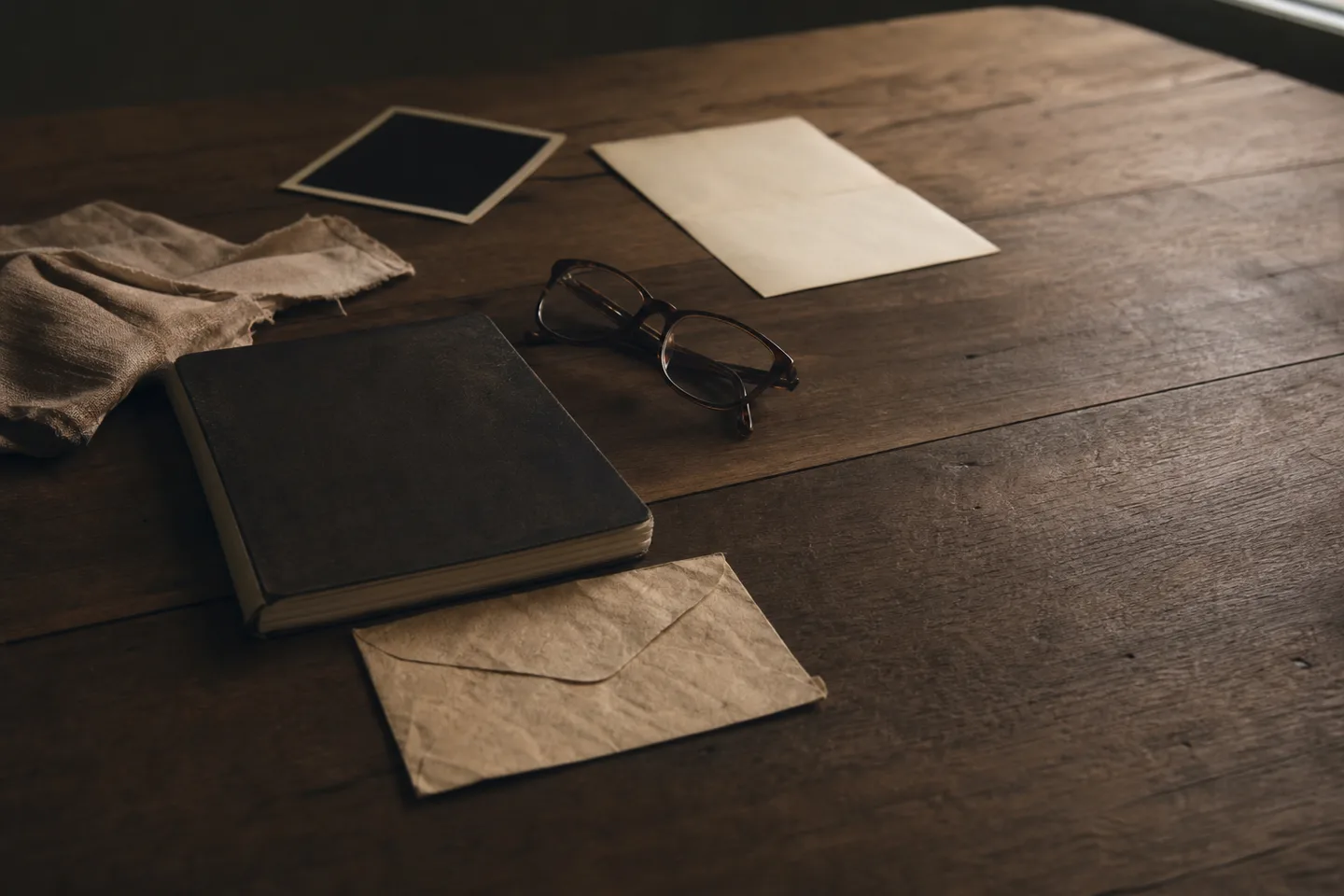 Carnet, enveloppe, lunettes et photographie retournée sur une table.
